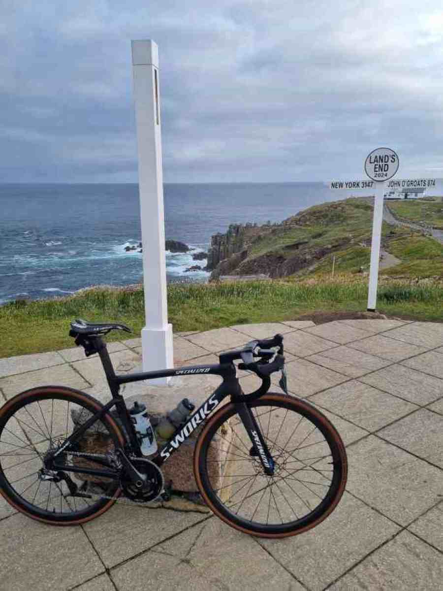 Bike leaning against a signpost at Land's End, with the cliffs and sea in the background.