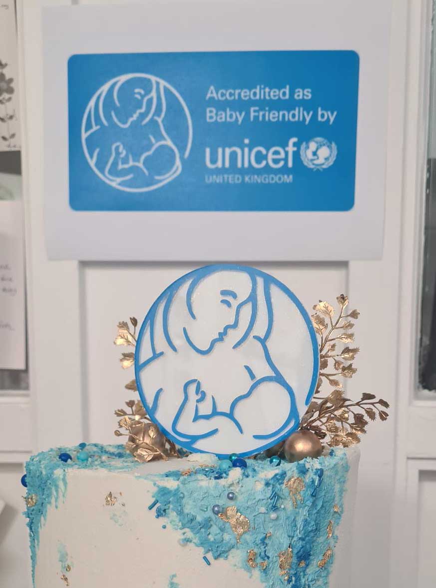 Cake with UNICEF baby friendly logo icing under wall sign for accreditation
