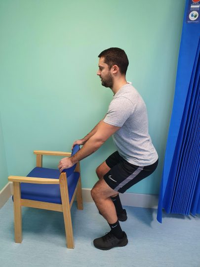 Person standing hip width apart and doing a half squat exercise