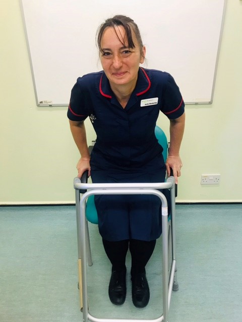 Patient standing in front of a chair with both hands on a walking frame directly in front of the chair.