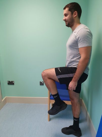 Person doing a hip flexion exercise using a chair for support