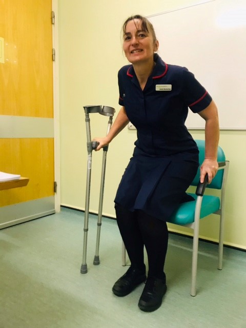 Patient rising from a chair with one hand on a pair of crutches and their other hand on the arm of the chair.