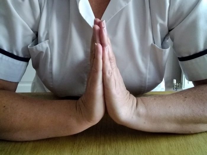 Person resting their forearms on a table and bringing their hands together in a prayer position
